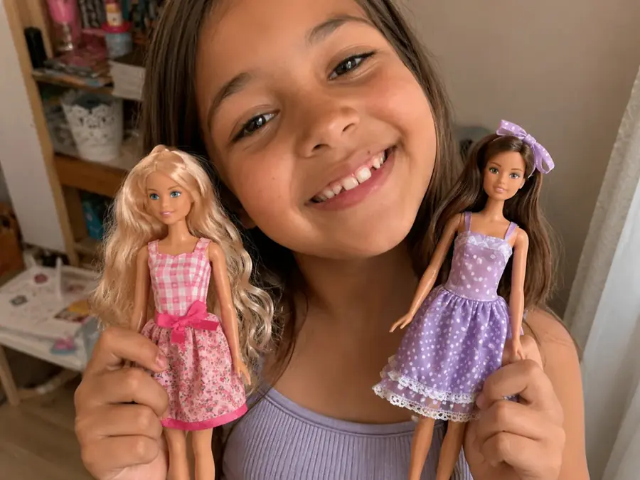 Menina segurando duas fashion dolls com vestidos artesanais